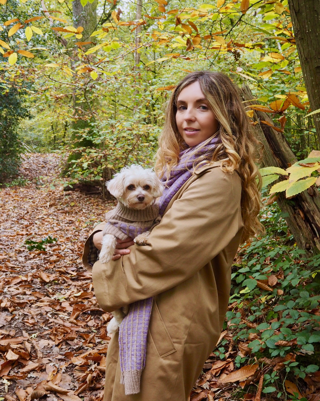 Woman in an autumn wood holding a small dog in a purple merino jumper
