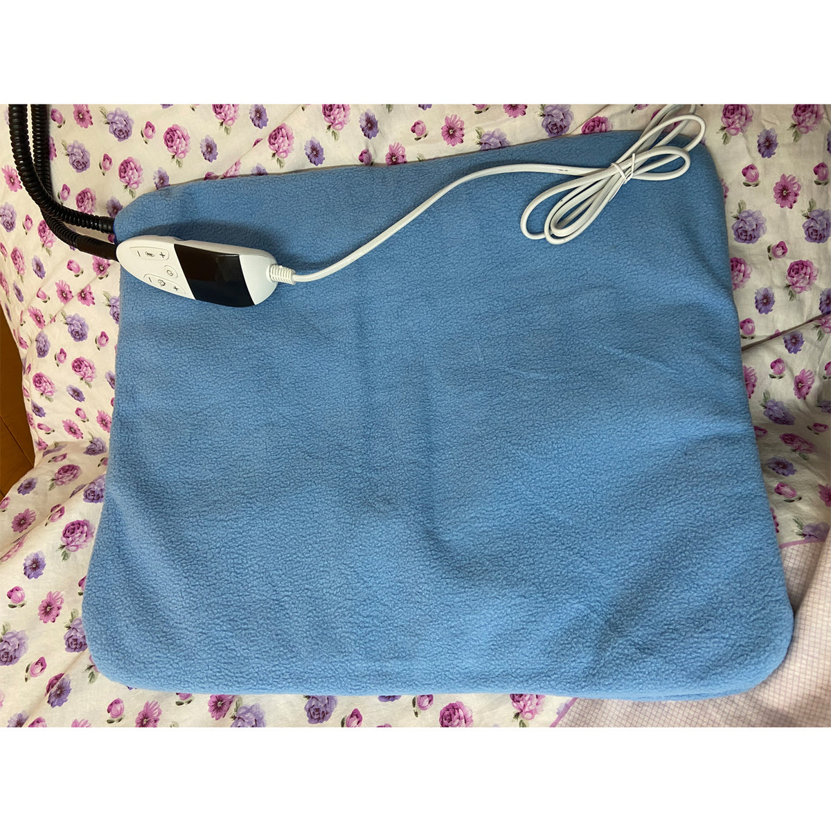 Blue fleece heated pad with cable and controller on a floral bedspread
