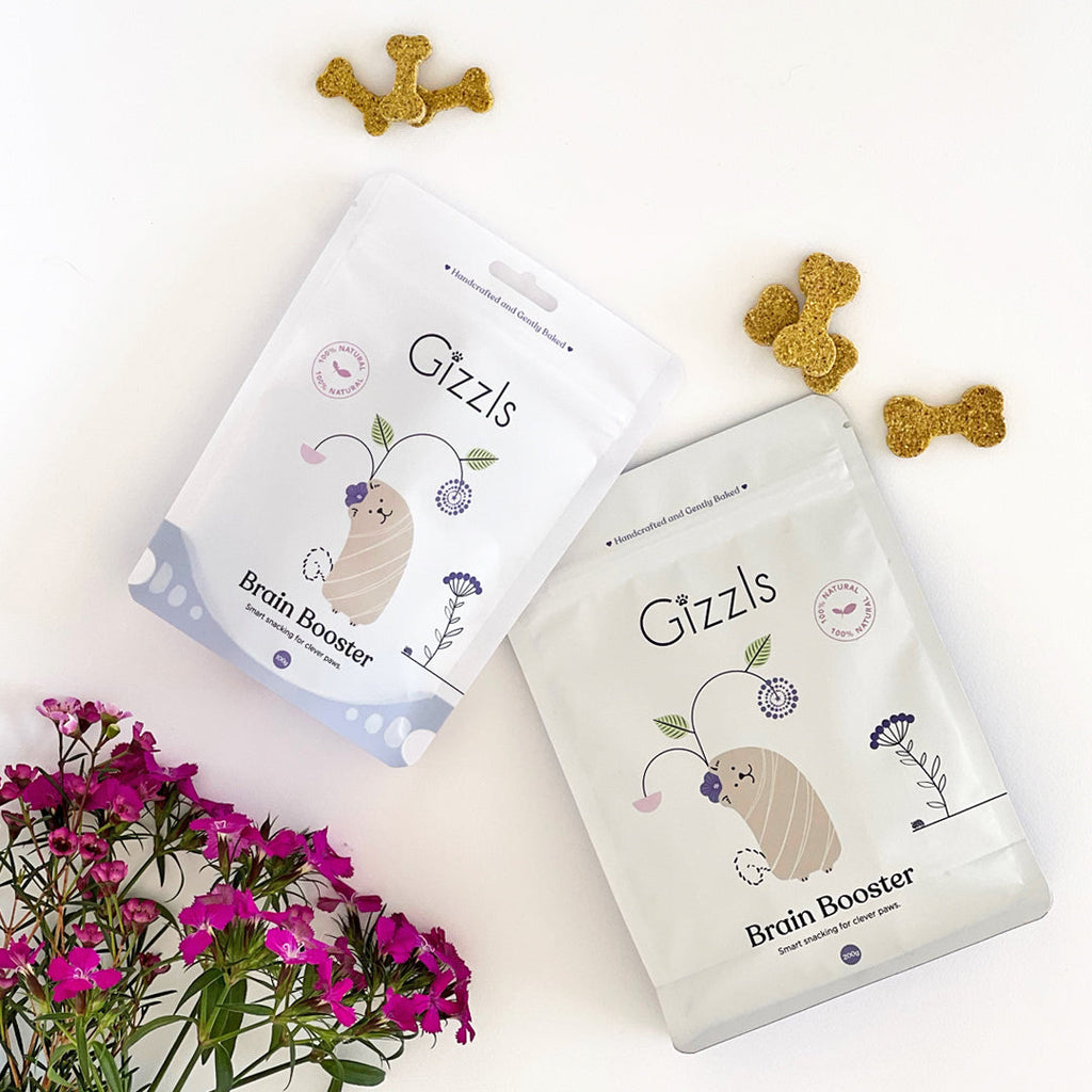 Two Gizzls Brain Booster pouches flat-lay with bone biscuits and pink flowers