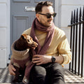 Man in a burgundy wool scarf sitting on steps with a dachshund in a matching jumper