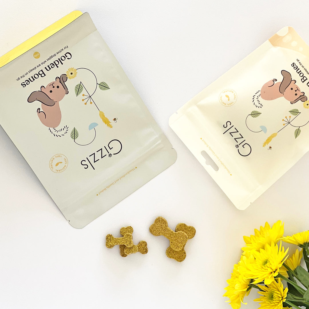 Two Gizzls Golden Bones pouches flat-lay with turmeric biscuits and yellow flowers