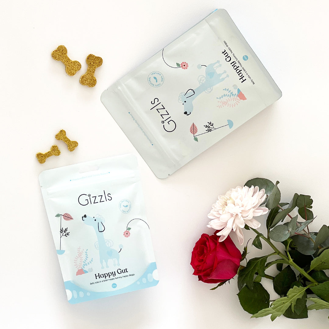 Two Gizzls Happy Gut pouches flat-lay with bone biscuits, rose and white flower