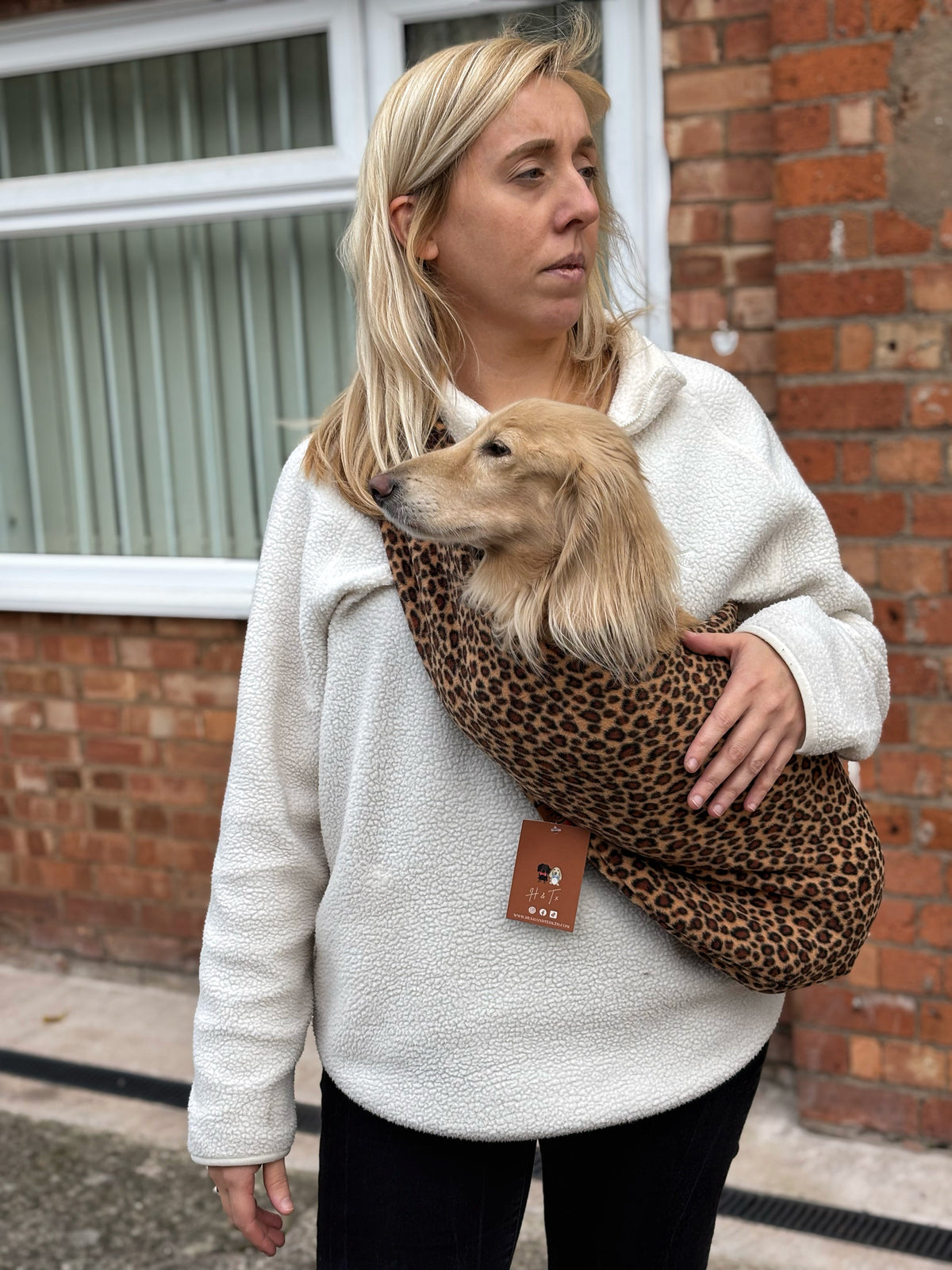 Woman carrying a cream long-haired dachshund in an orange leopard Patterned Fleece Dog Sling