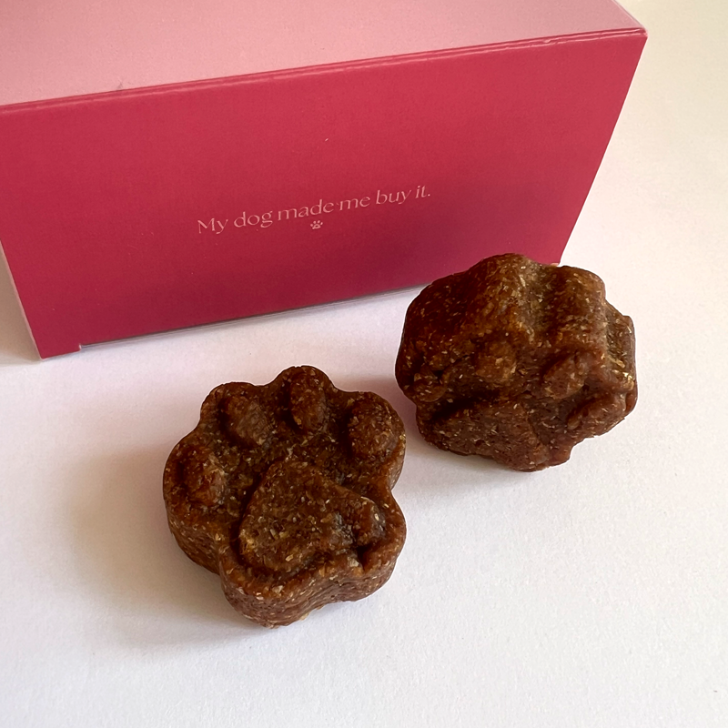 Two soft paw-shaped My Dog Made Me Buy It peanut butter & strawberry treats by a red box
