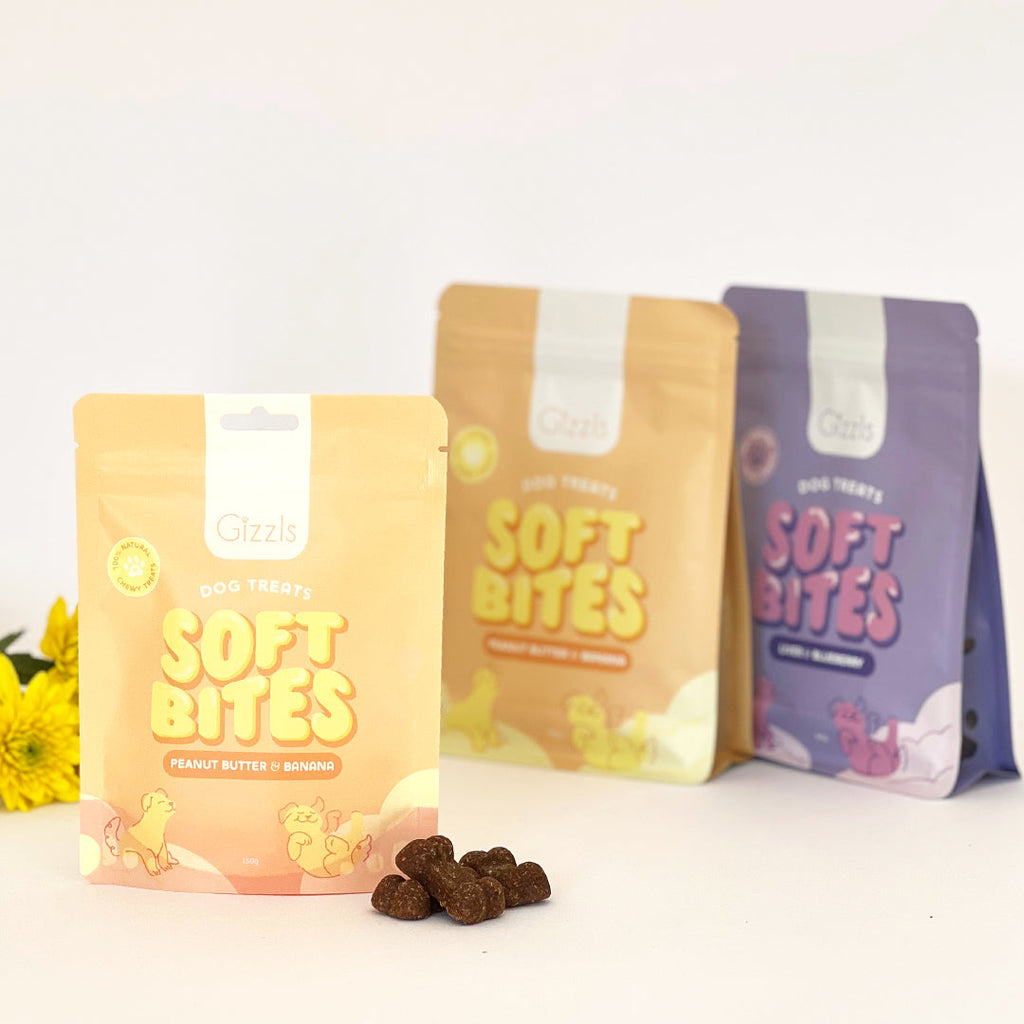 Three Soft Bites pouches in yellow and purple with treats and yellow flowers