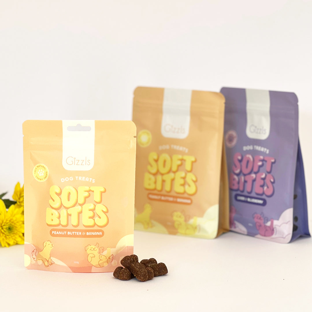Three Soft Bites pouches in yellow and purple with treats and yellow flowers