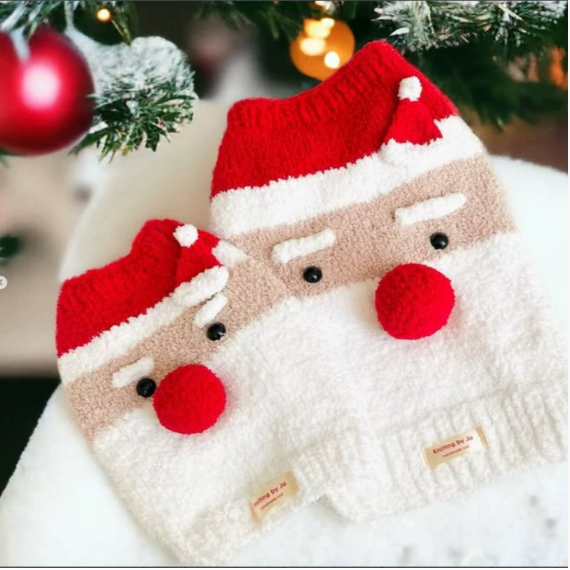 Two fuzzy Santa dog jumpers by a Christmas tree
