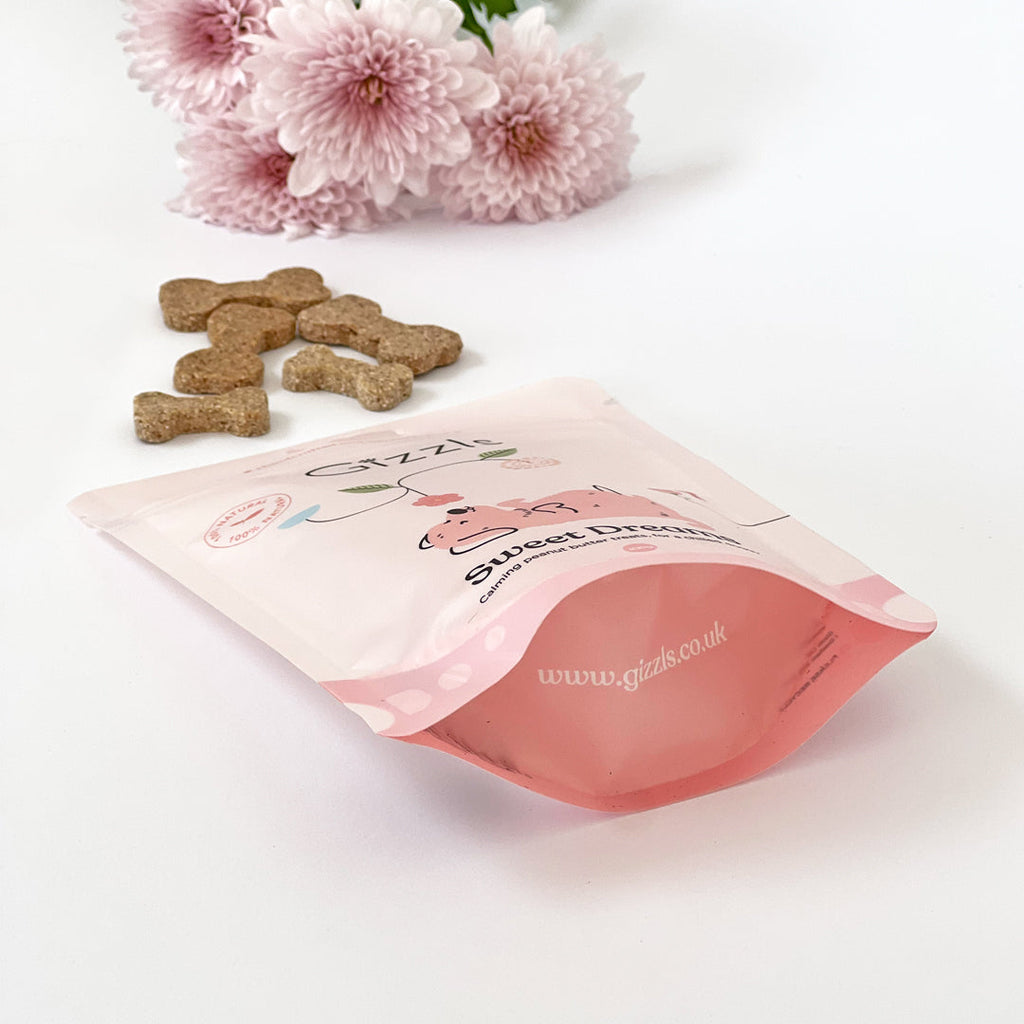 Open Sweet Dreams Small Dog Treats pouch with bone biscuits spilling out beside pink flowers