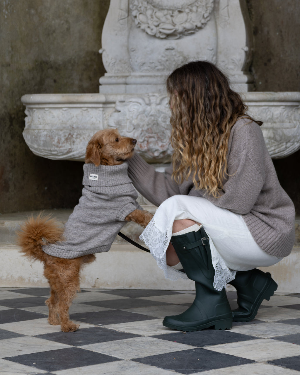 Woman in wellies kneeling with a golden dog in a grey wool jumper