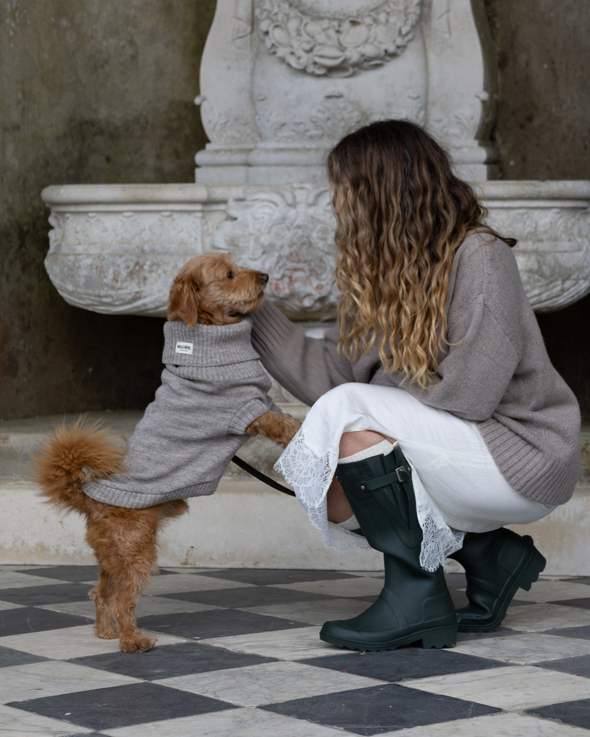 Woman in wellies kneeling with a golden dog in a grey wool jumper