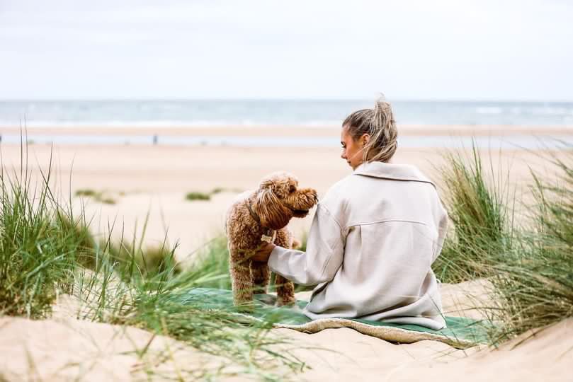 Woman and Cockapoo sitting on the Richmond green blanket in beach dunes