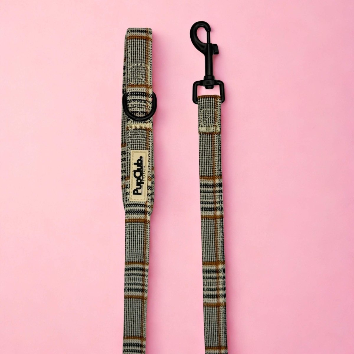 Foxbury Plaid Dog Lead laid flat on pink, showing the brown and cream check handle and black clip