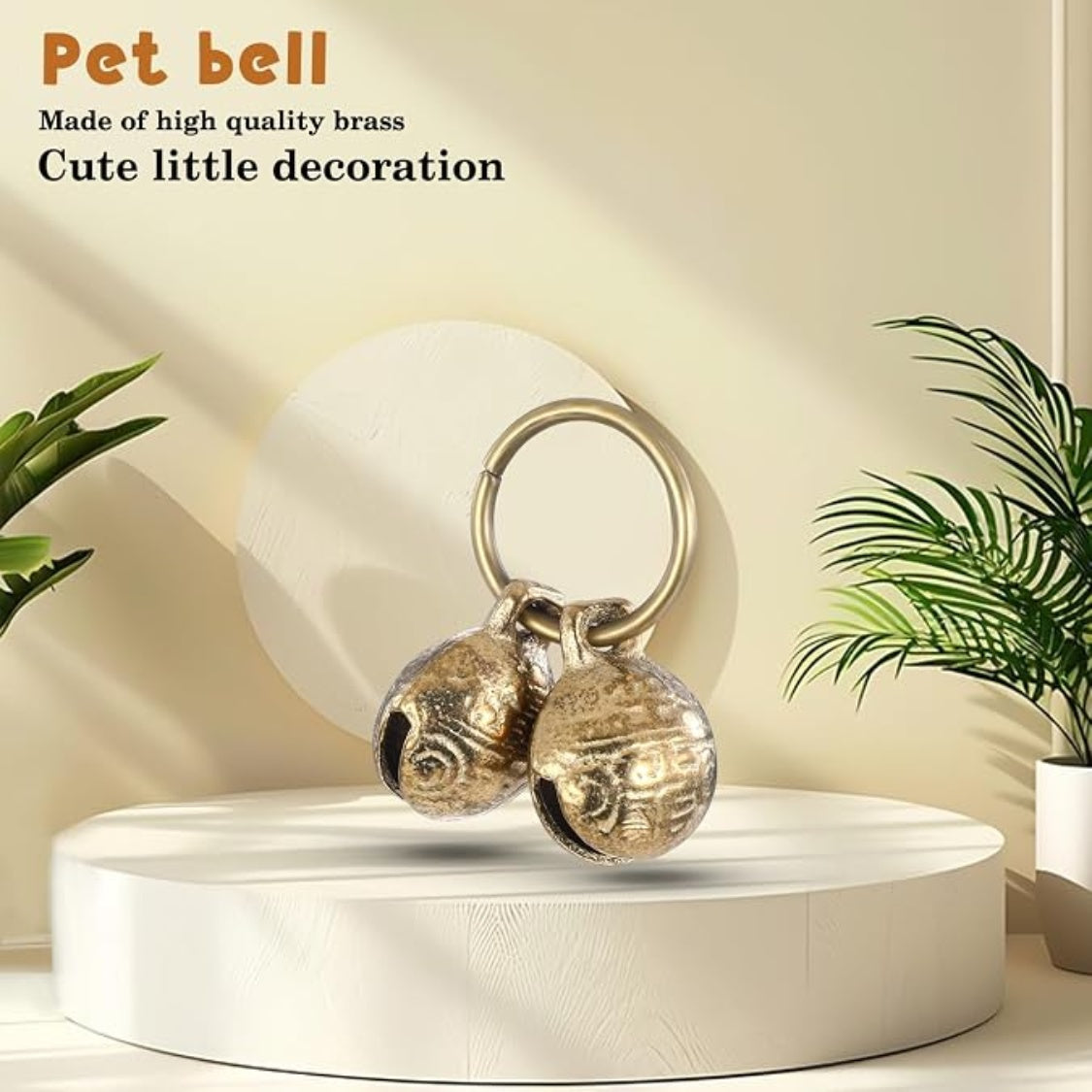 Pair of round brass pet bells on a ring, on a white display stand