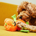 Apricot doodle on a yellow sofa chewing the orange pumpkin plush toy with green leaf arms
