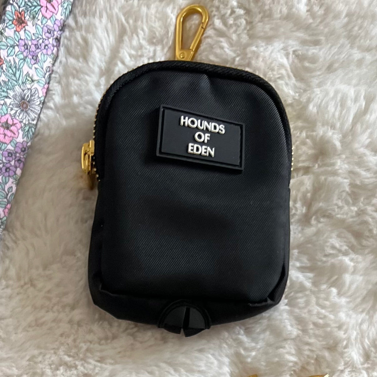 Black clip-on dog treat and poo bag pouch with gold clip on a fluffy rug