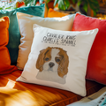 Off-white Cavalier King Charles Spaniel cushion on an orange sofa among teal, cream and red cushions