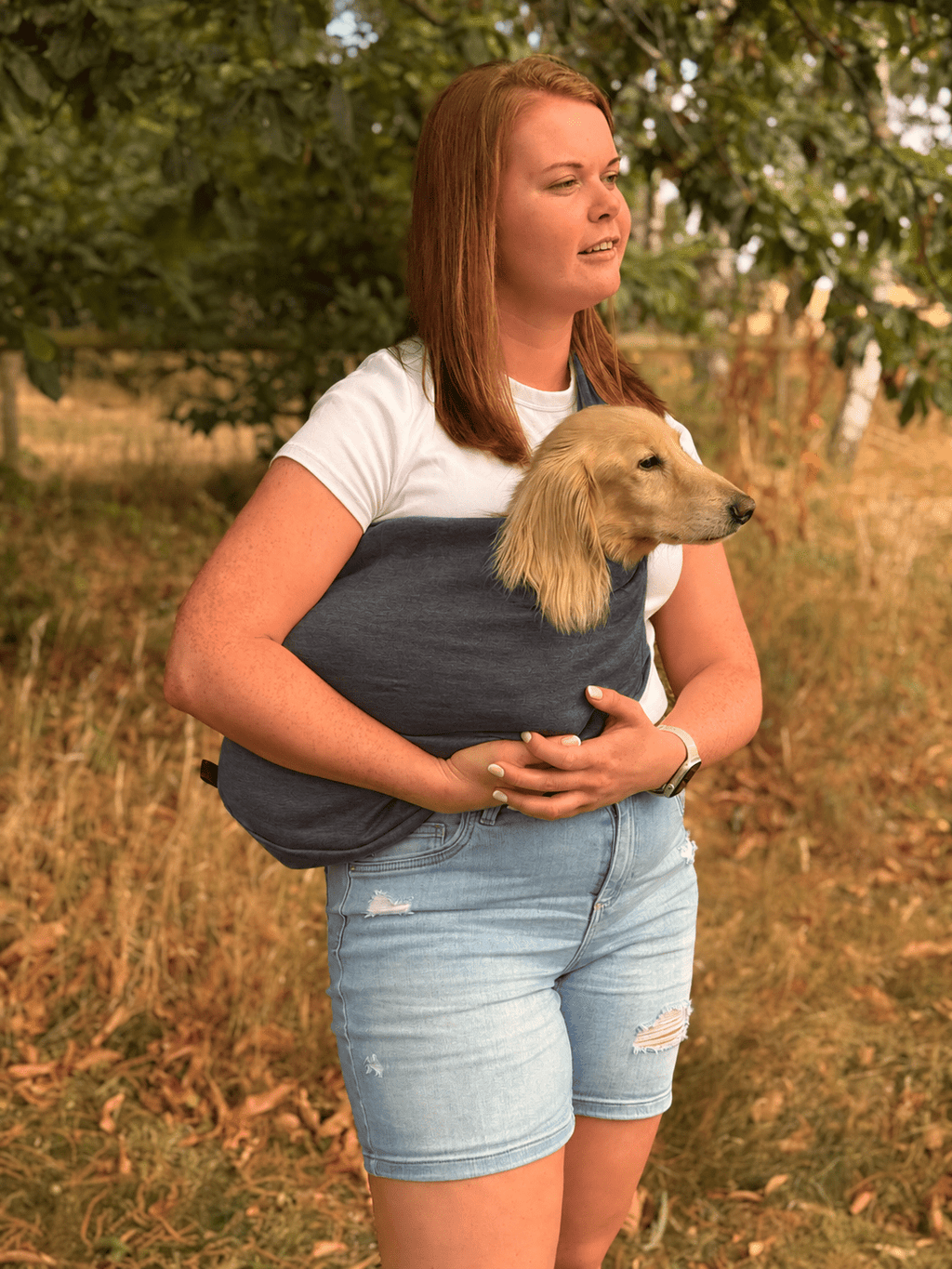 Woman in a field carrying a cream long-haired dog in a charcoal Lite Sweatshirt Dog Sling