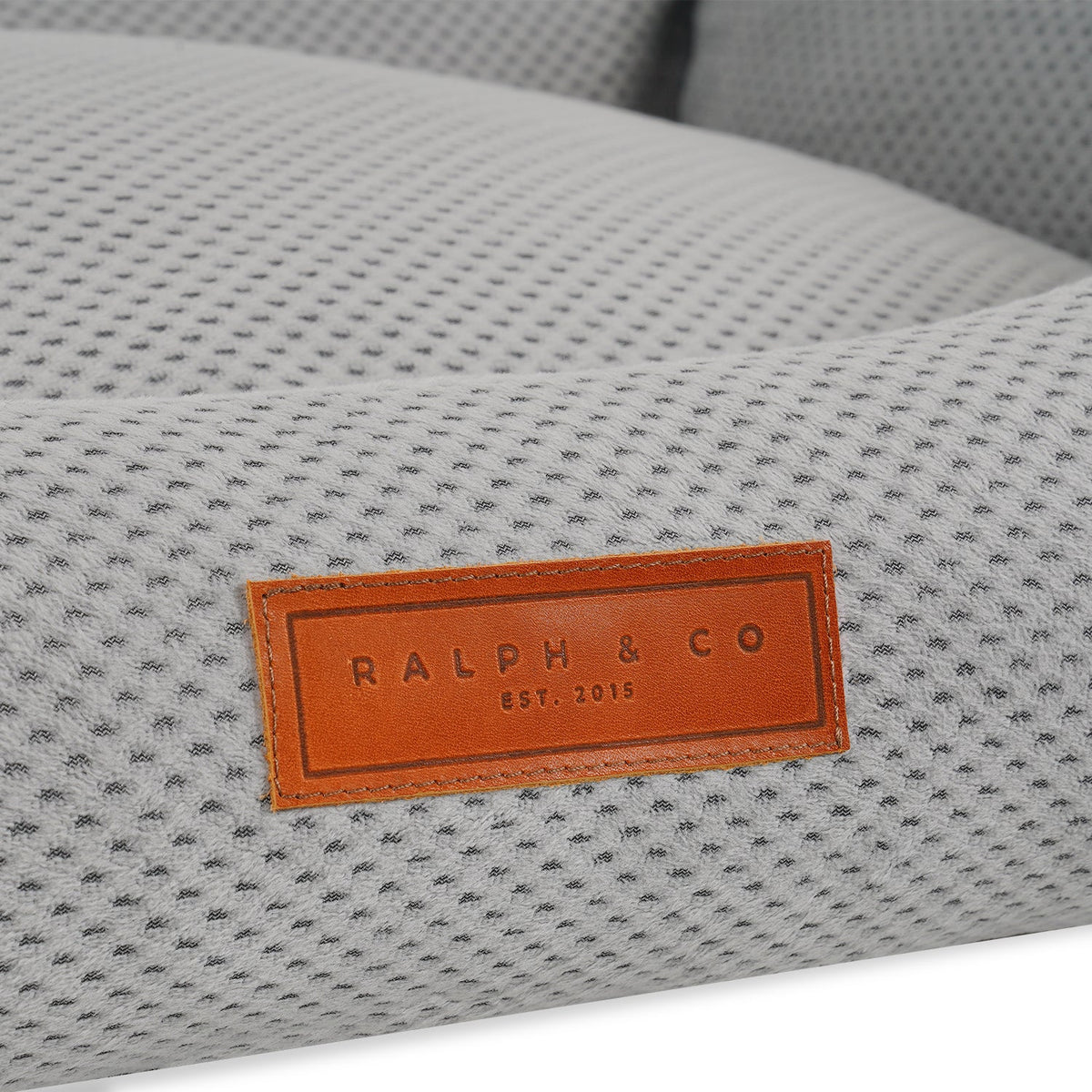 Close-up of the leather Ralph & Co badge on the grey knitted Highclere bed