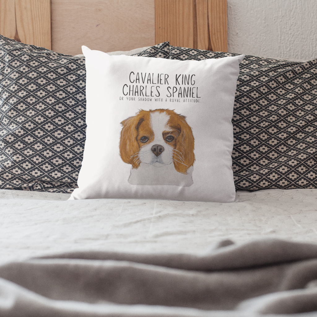 Cavalier King Charles Spaniel cushion on a bed in front of grey patterned pillows