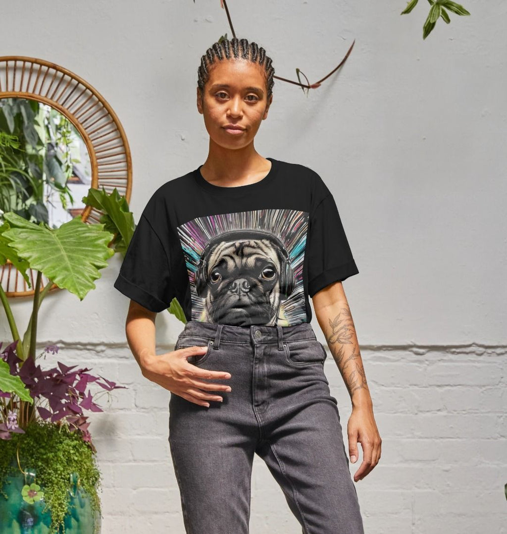 Woman in a black pug-in-headphones print T-shirt and grey jeans standing beside green plants