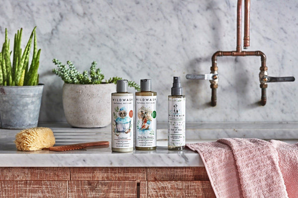 WildWash bottles on a marble counter with a natural sponge, wooden comb and pink towel