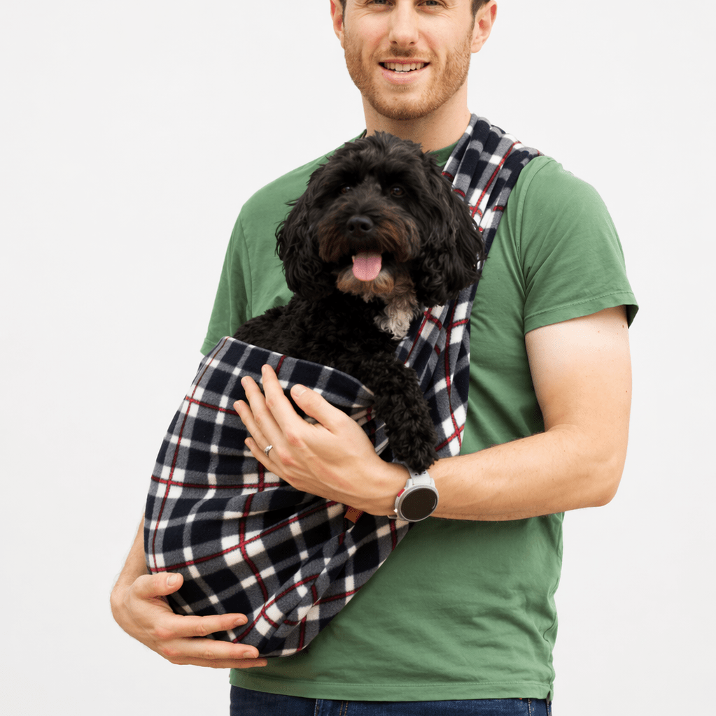 Man carrying a black cockapoo in a black and red check Patterned Fleece Dog Sling