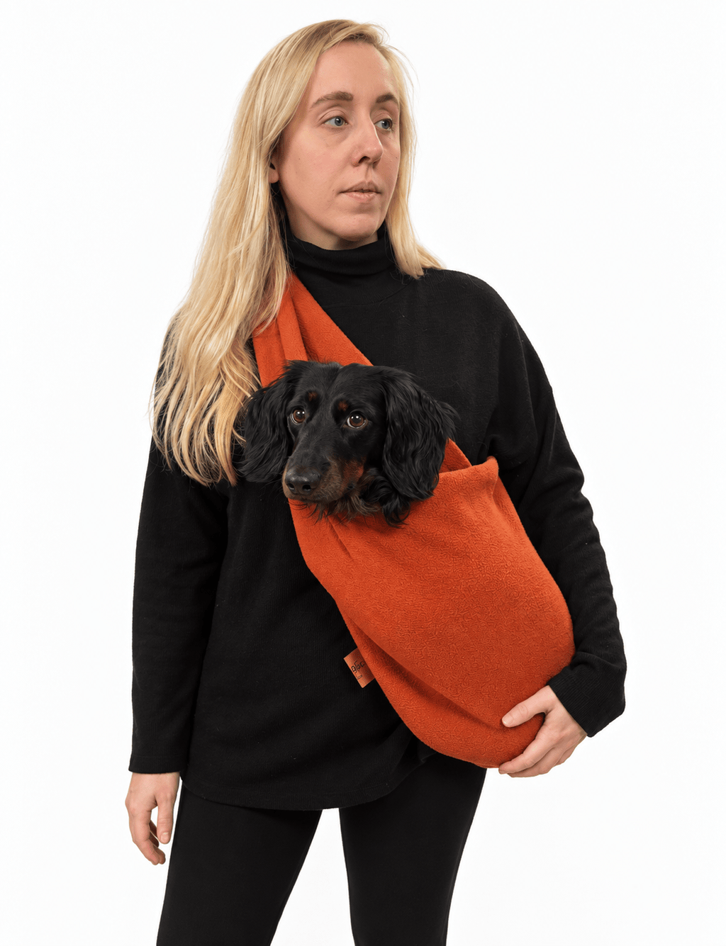 Woman wearing a rust orange Plain Fleece Dog Sling with a black long-haired dachshund